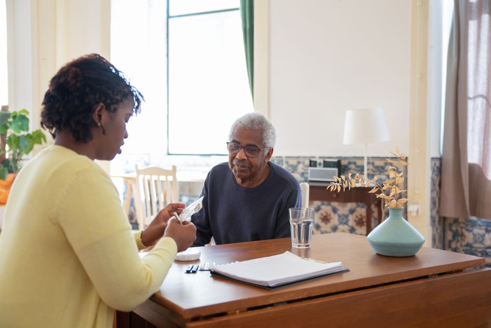 Stock photograph of a younger Black caregiver spending time with an older Black man in a bright home