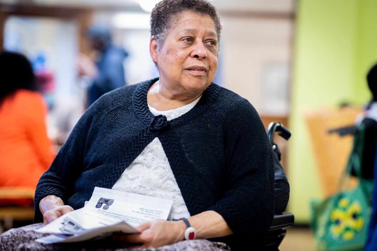 Illustrative stock portrait of an older Black woman holding reading material while seated in a wheelchair