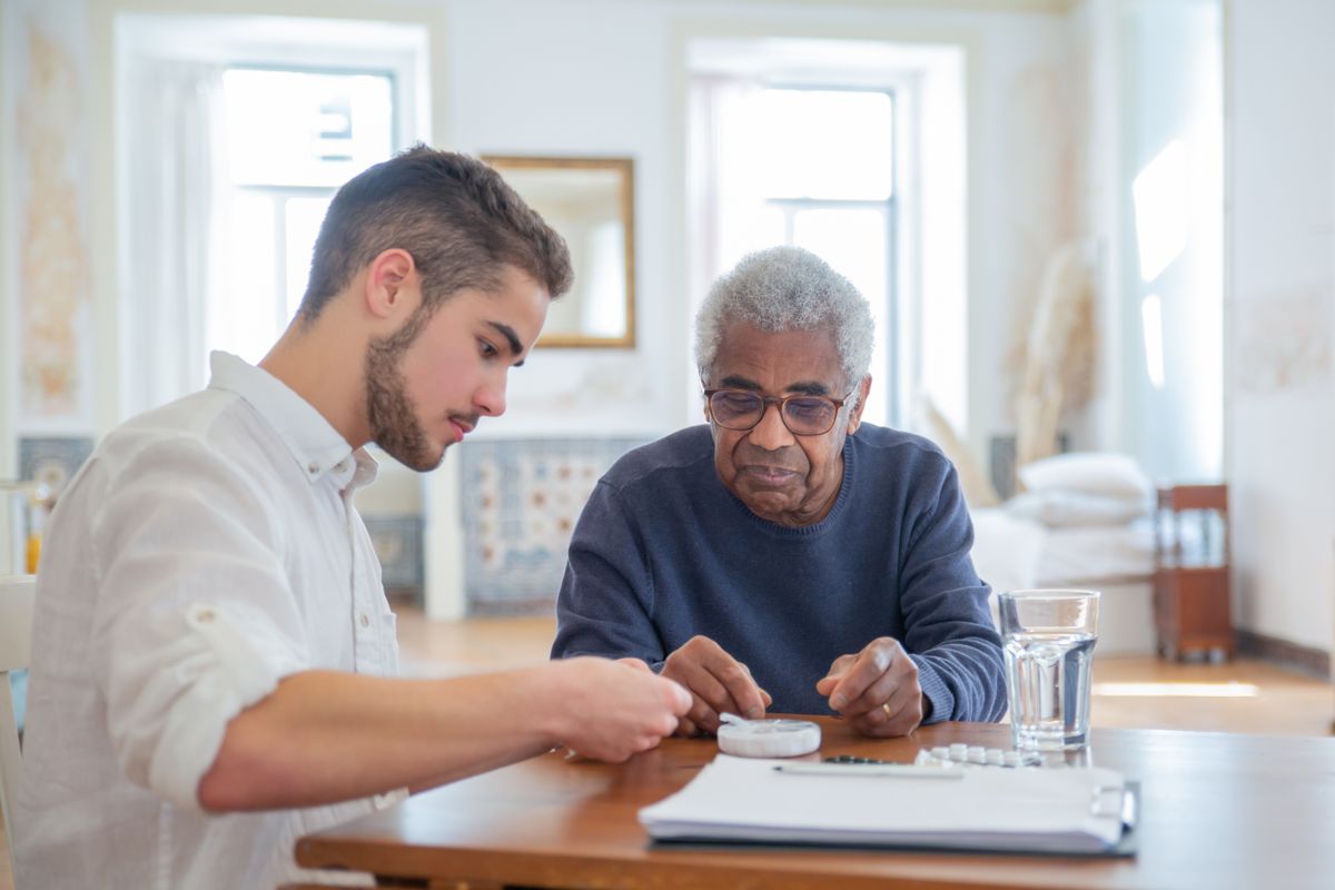 Stock photograph of a young male caregiver helping an older Black man at home