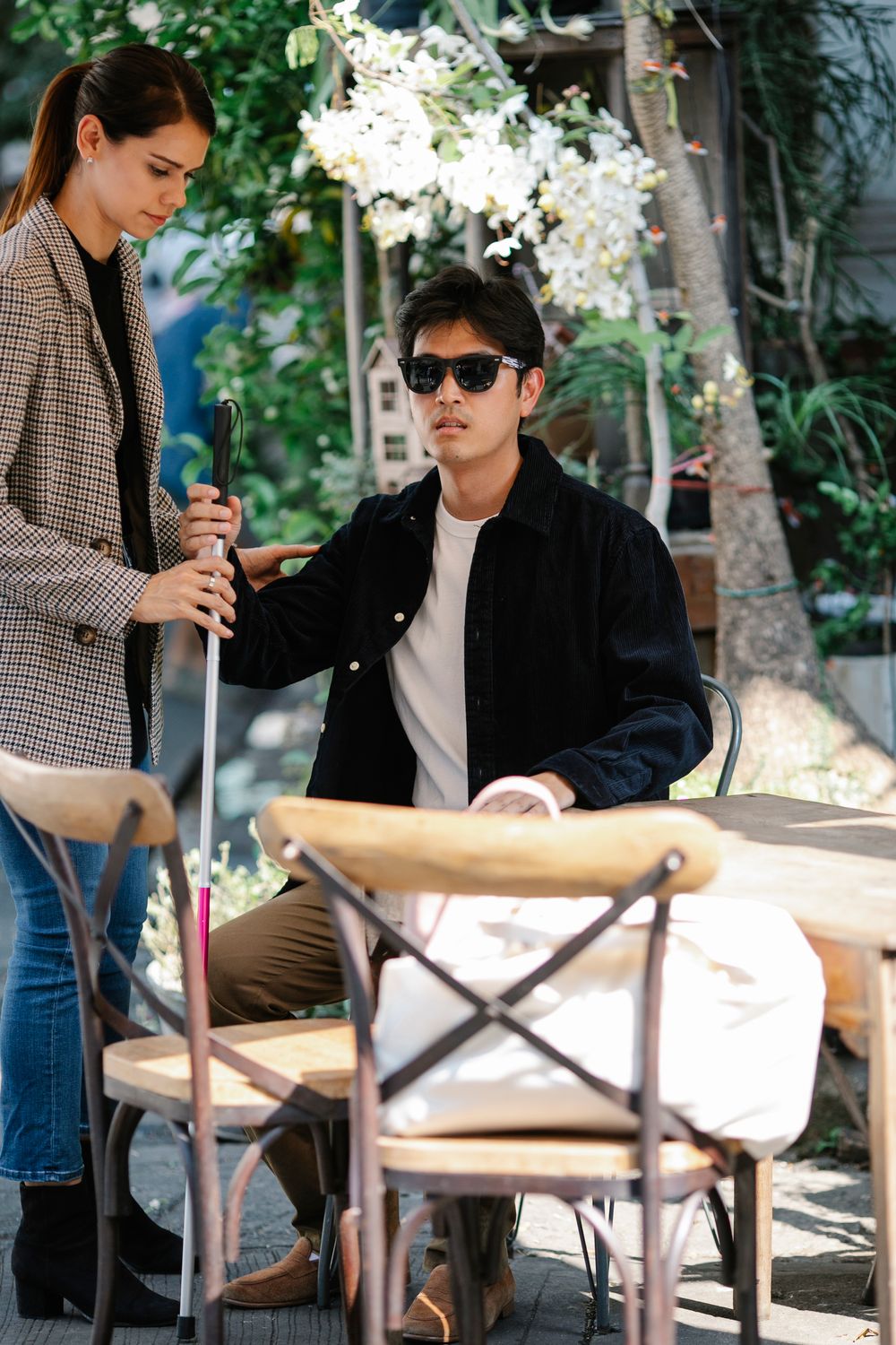 Stock photograph of an Asian woman supporting an Asian man using a white cane outdoors